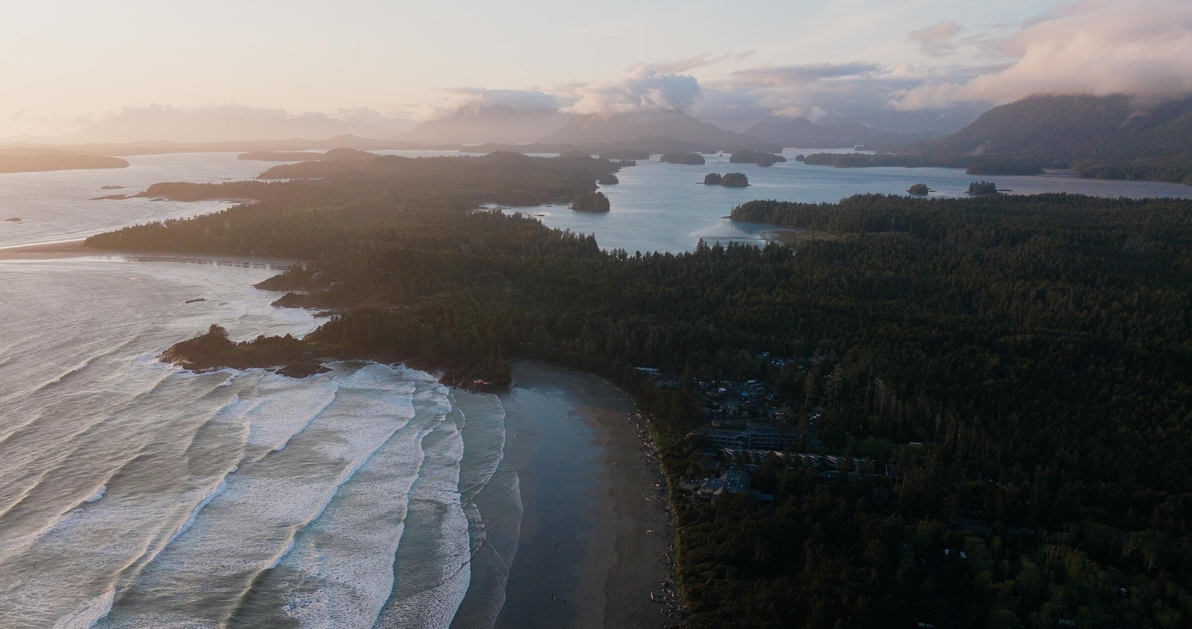 Waves wrapping into a beach along the forested coast near Tofino, seen from the air