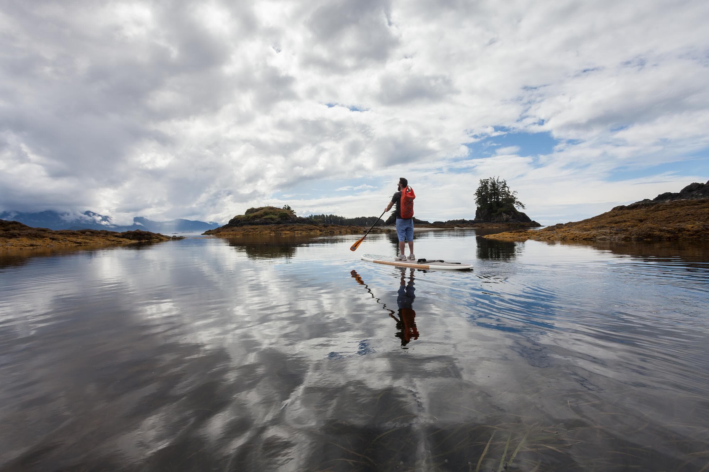 A paddleboarder on still, reflecting water near Kyuquot Sound in summer