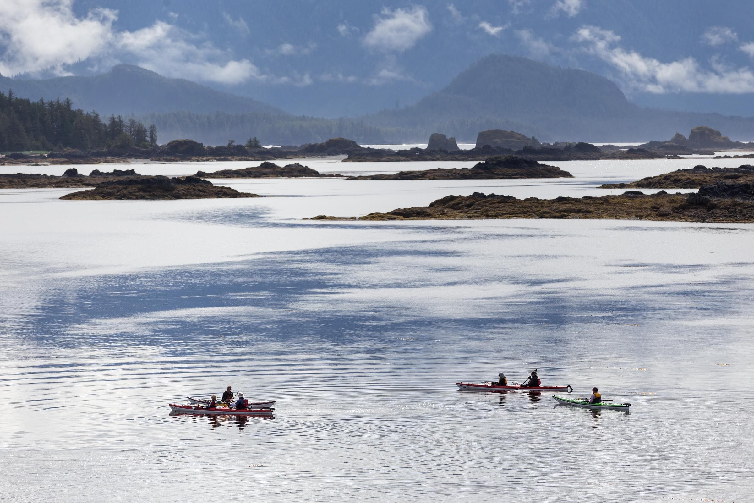 Kayakers crossing calm water among the islets of Kyuquot Sound