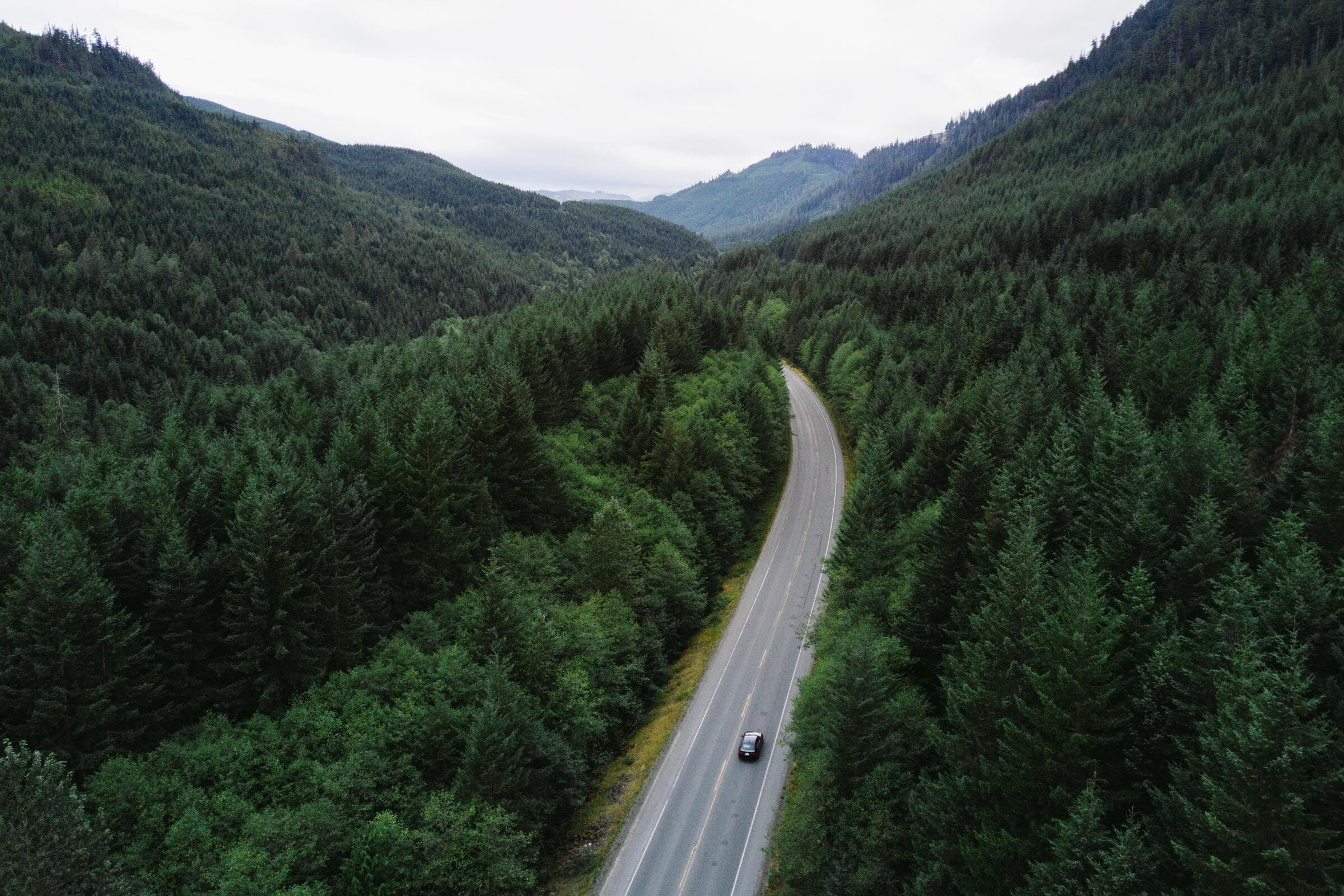 A car on a highway through forested mountains, seen from above